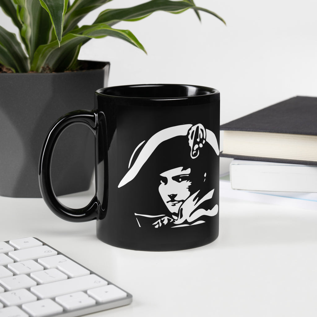 Black mug with a white graphic design on a desk with a plant and books in the background