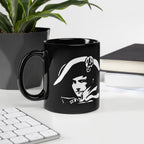 Black mug with a white graphic design on a desk with a plant and books in the background