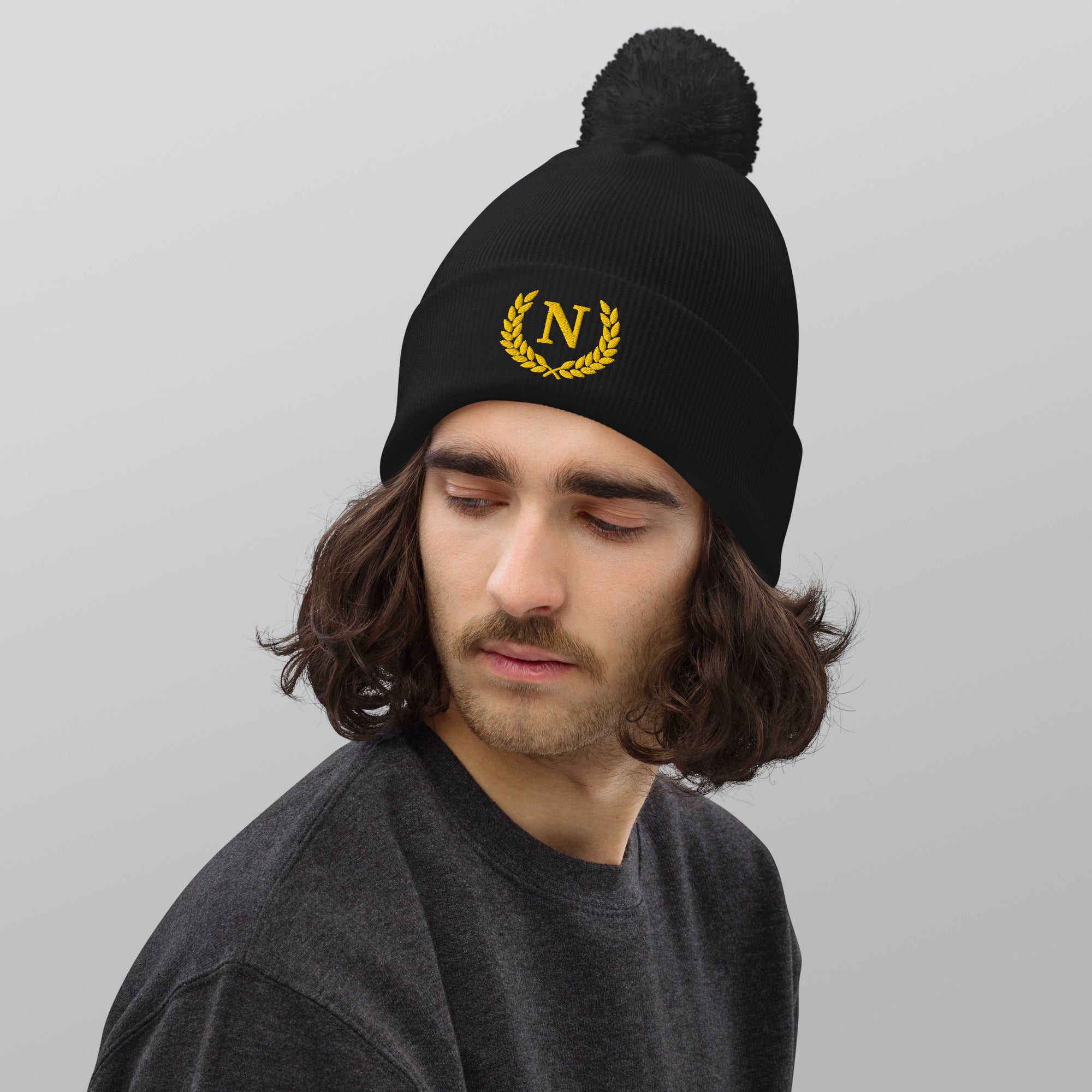 Person wearing a black beanie with a yellow logo on a gray background