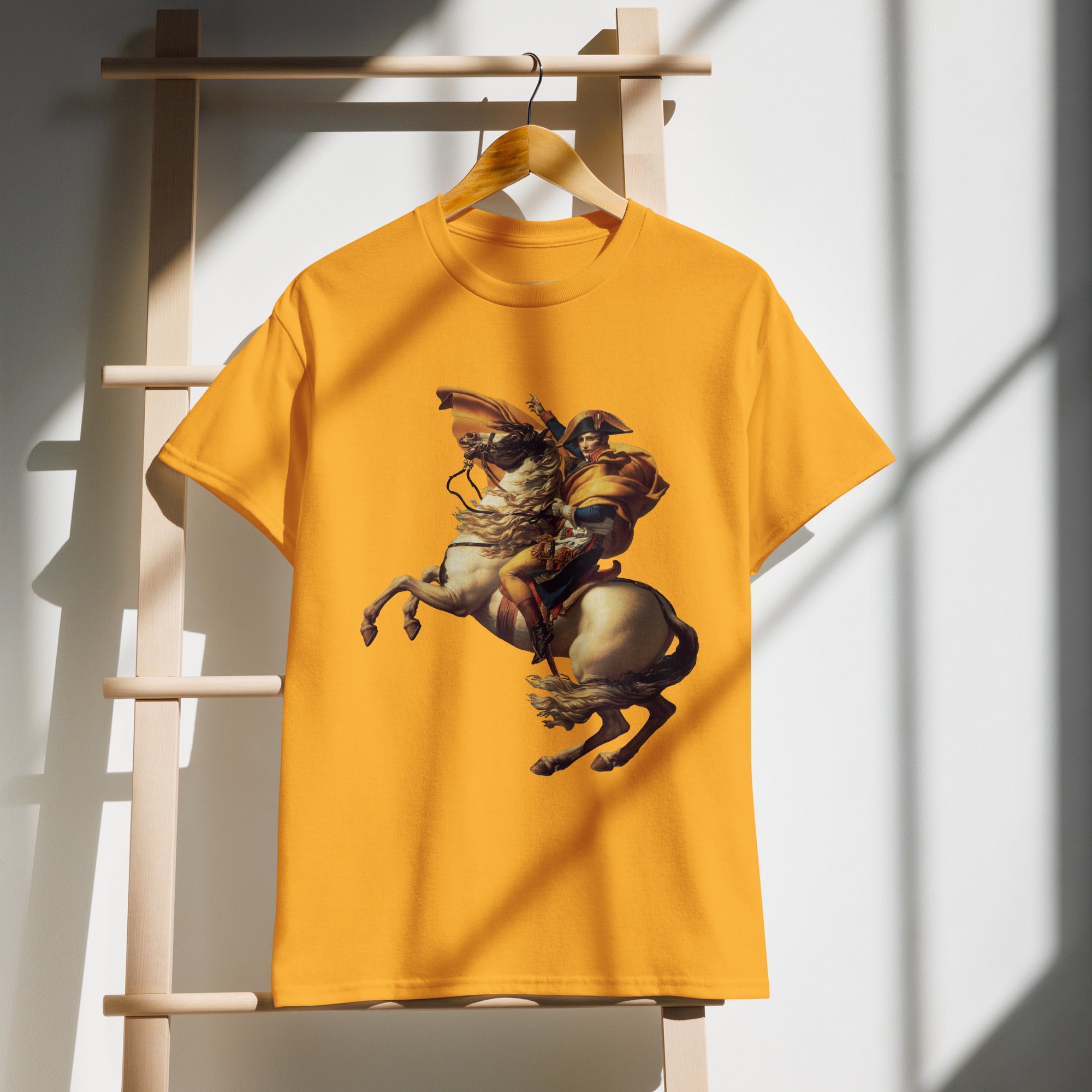 Yellow t-shirt with a graphic of a person riding a horse on a wooden hanger against a white wall.